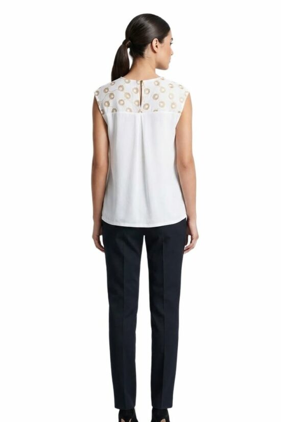 Back view of a woman wearing a white sleeveless blouse with a patterned yoke and navy dress pants