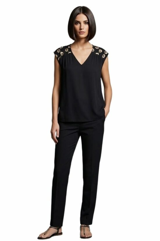 Model wearing a black V neck top with decorative shoulder cutouts and matching black pants standing in sandals