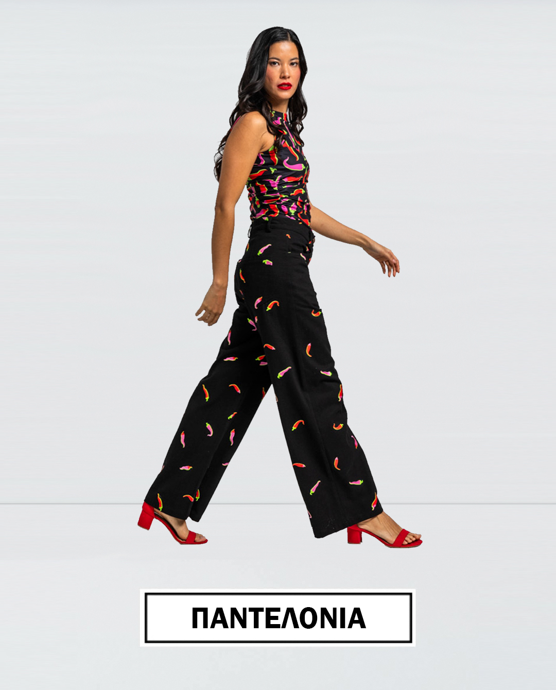 Model walking in black wide leg pants with a colorful small pattern paired with a matching sleeveless top and red heeled sandals ΠΑΝΤΕΛΟΝΙΑ label shown at the bottom